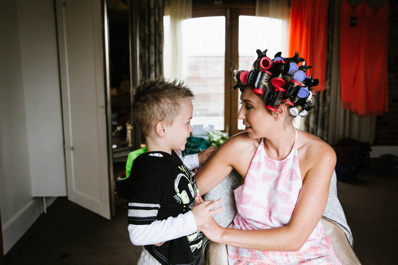 bride in hair curlers giving her son a cuddle in dressing room at mythe barn