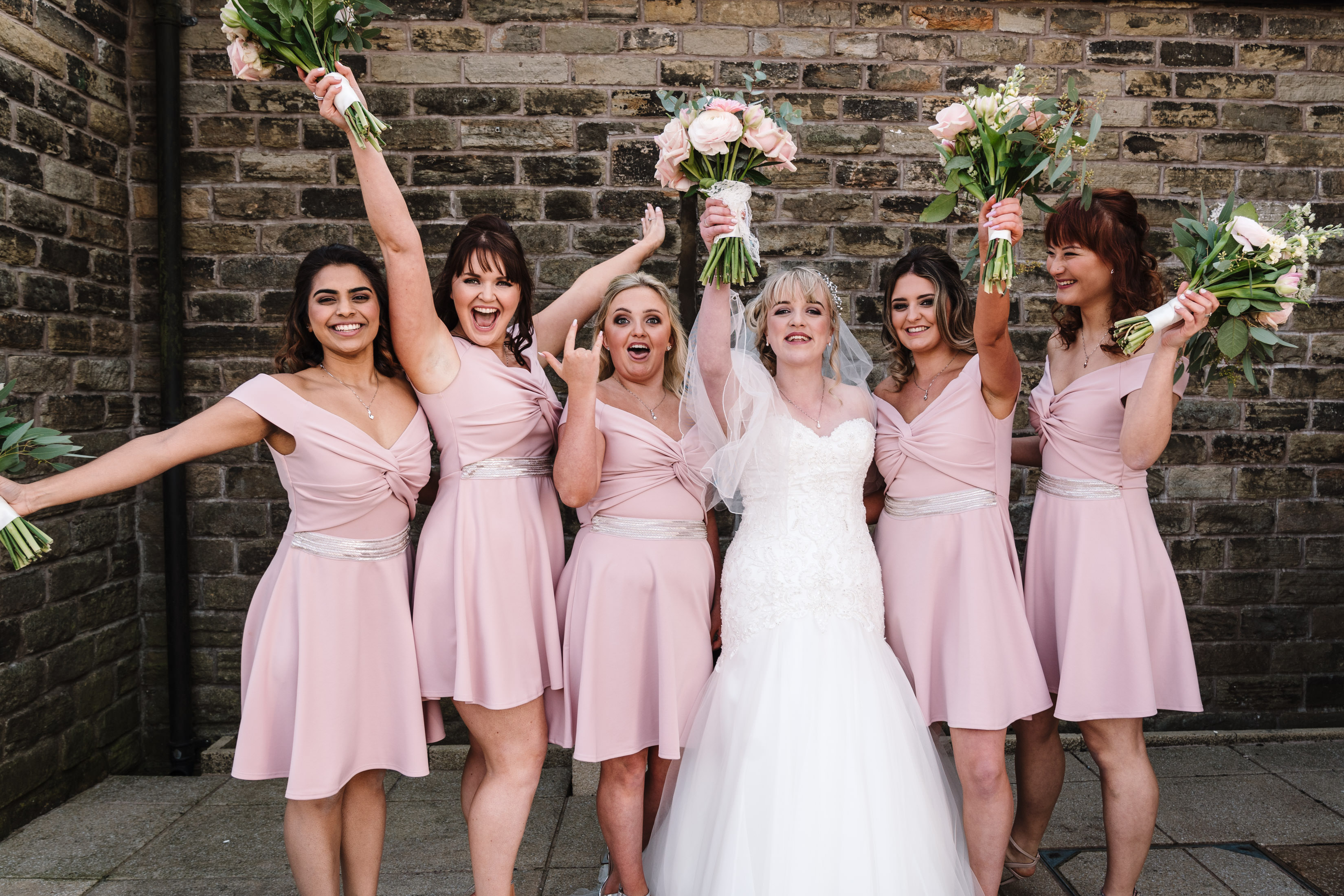 Bridesmaids holding up bouquets and posing for photograph