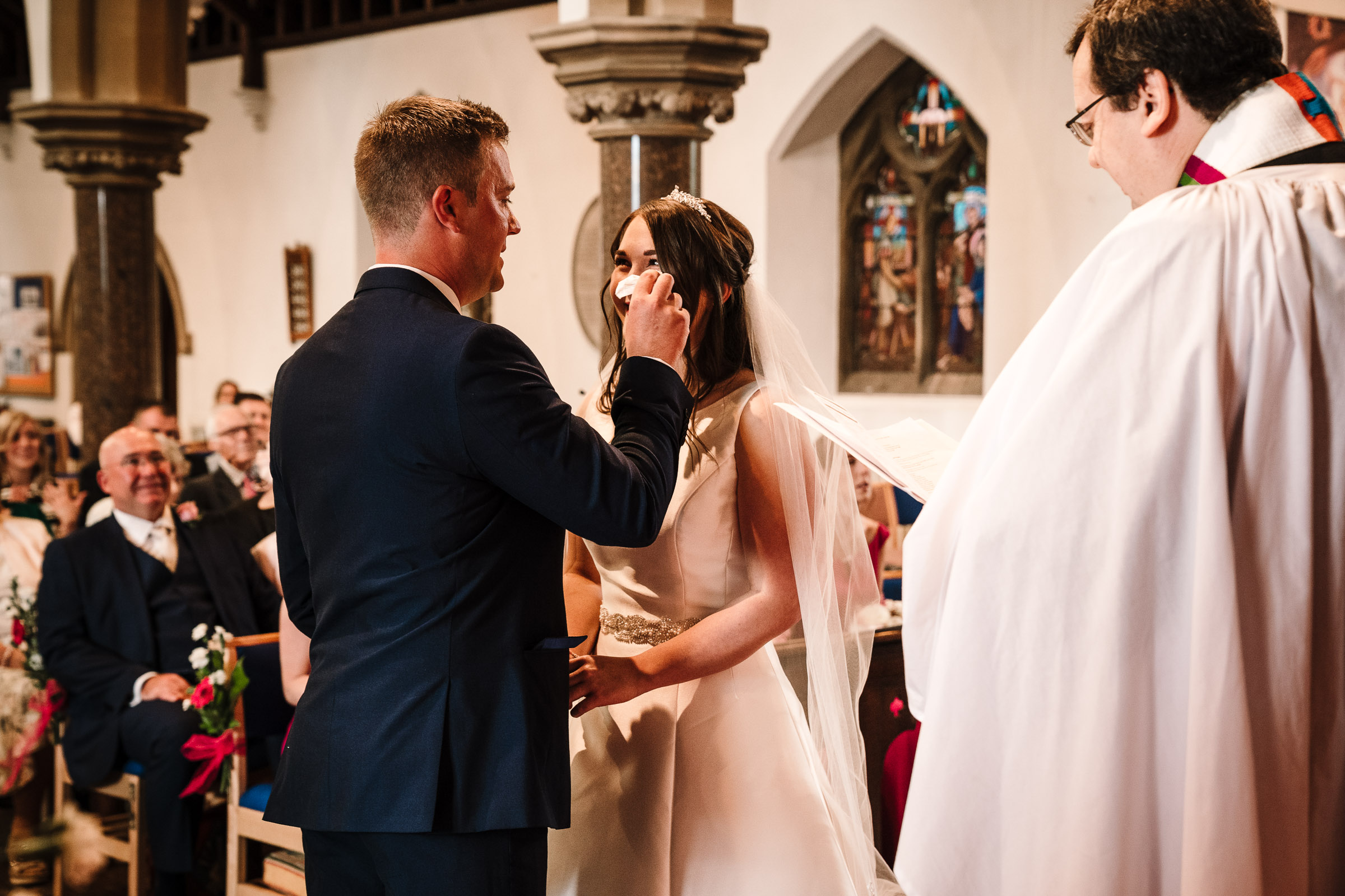 groom wiping tear away from brides face during wedding ceremony